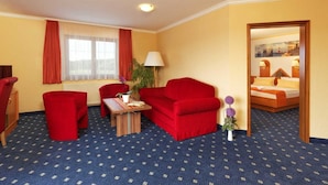 Ein Hotelzimmer mit rotem Sofa, einem kleinen Tisch mit Lampe, einem Fenster mit Vorhängen und einem Bett mit Blick auf die Stadt.