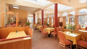 A restaurant with high ceilings, wooden beams, and large windows. Tables are set with yellow tablecloths and red chairs. - Apartment handicapped accessible (balcony or terrace) - Hanse-Kogge Hotel & (Koserow)