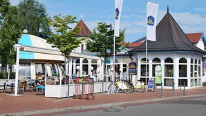 A traditional European building with a black roof and white walls, a small outdoor seating area with tables and chairs, and a sign indicating a reception area. - Apartment handicapped accessible (balcony or terrace) - Hanse-Kogge Hotel & (Koserow)