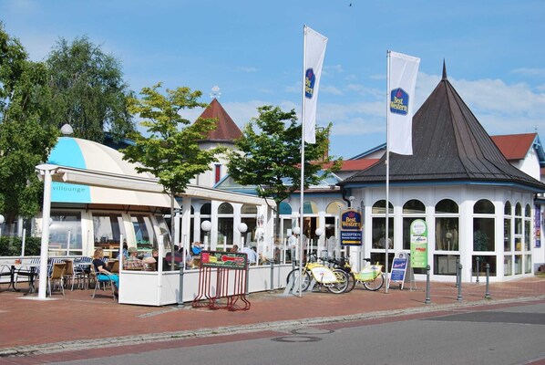A traditional European building with a black roof and white walls, a small outdoor seating area with tables and chairs, and a sign indicating a reception area.