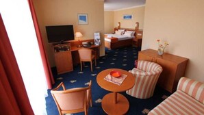 A hotel room with a bed, a desk with a TV, a chair, a small table, and a sofa. - Double room - Hanse-Kogge Hotel & Restaurant (Koserow)