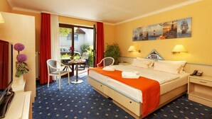 Habitación de hotel con cama, dos mesitas de noche, un escritorio, una silla, una pequeña mesa y una ventana con cortinas rojas.