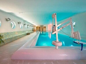 A swimming pool with a water slide and a changing room area with mirrors and a tiled wall.