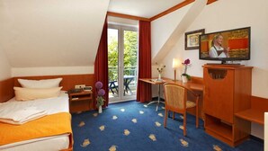 A hotel room with a bed, a desk, a chair, a television, and a balcony with red curtains. - Single room Comfort (balcony or terrace) - Hanse-Kogge Hotel & Restaurant (Koserow)