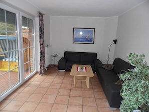 A living room with a sofa, a small table, a potted plant, a framed picture on the wall, and a sliding glass door leading to an outdoor area.