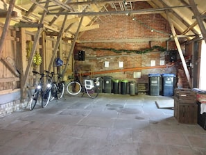 A rustic barn interior with bicycles, trash bins, and a brick wall.