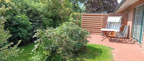 A patio with a table and chairs, surrounded by a brick wall and dense foliage.