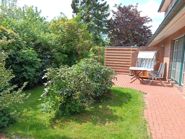 En patio med et bord og stole, omgivet af en murstensmur og frodig beplantning.