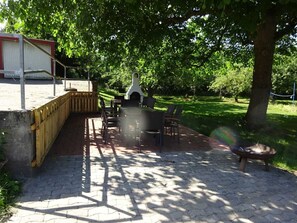 En udendørs terrasse med grill, spisebord og stole.