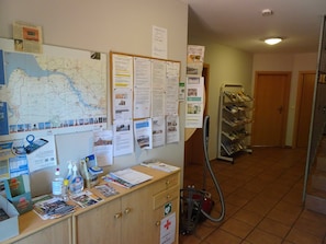 A reception area with a map, informational posters, a vacuum cleaner, and a shoe rack.