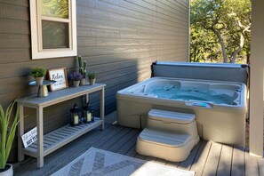 Een hottub op een houten terras, met een kleine tafel en potplanten.