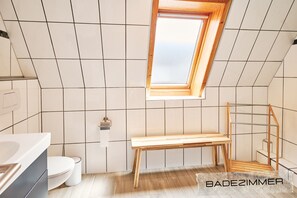 Une petite salle de bain moderne avec des murs recouverts de carreaux blancs, un banc en bois et un puits de lumière.
