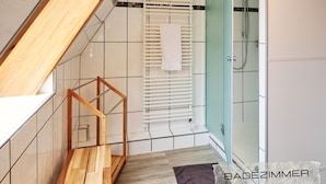 Ein modernes Badezimmer mit einer Duschkabine aus Glas, einer Holztreppe und einem weißen Handtuch an einer Heizung.
