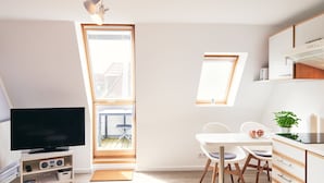 Eine moderne, kompakte Wohnung mit Fernseher, Küchenzeile, Essbereich und einem großen Oberlicht.