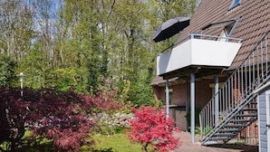 Ein Wohngebäude mit Balkon, Treppe und Garten mit verschiedenen Bäumen.