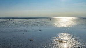 Ein Strand mit Menschen, die gehen und stehen, und ein Schiff in der Ferne.