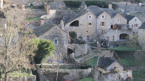 Un edificio de piedra con varias ventanas y un arco central, rodeado de terrazas y vegetación.