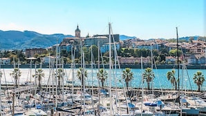 Eine Marina mit zahlreichen vertäuten Booten, ein markantes Gebäude mit einem Turm im Hintergrund und eine hügelige Landschaft.