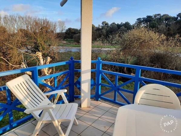 A terrace with a blue railing, two white chairs, and a table with a logo.
