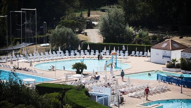 Ett poolområde med flera pooler, solstolar, parasoller och en liten byggnad.