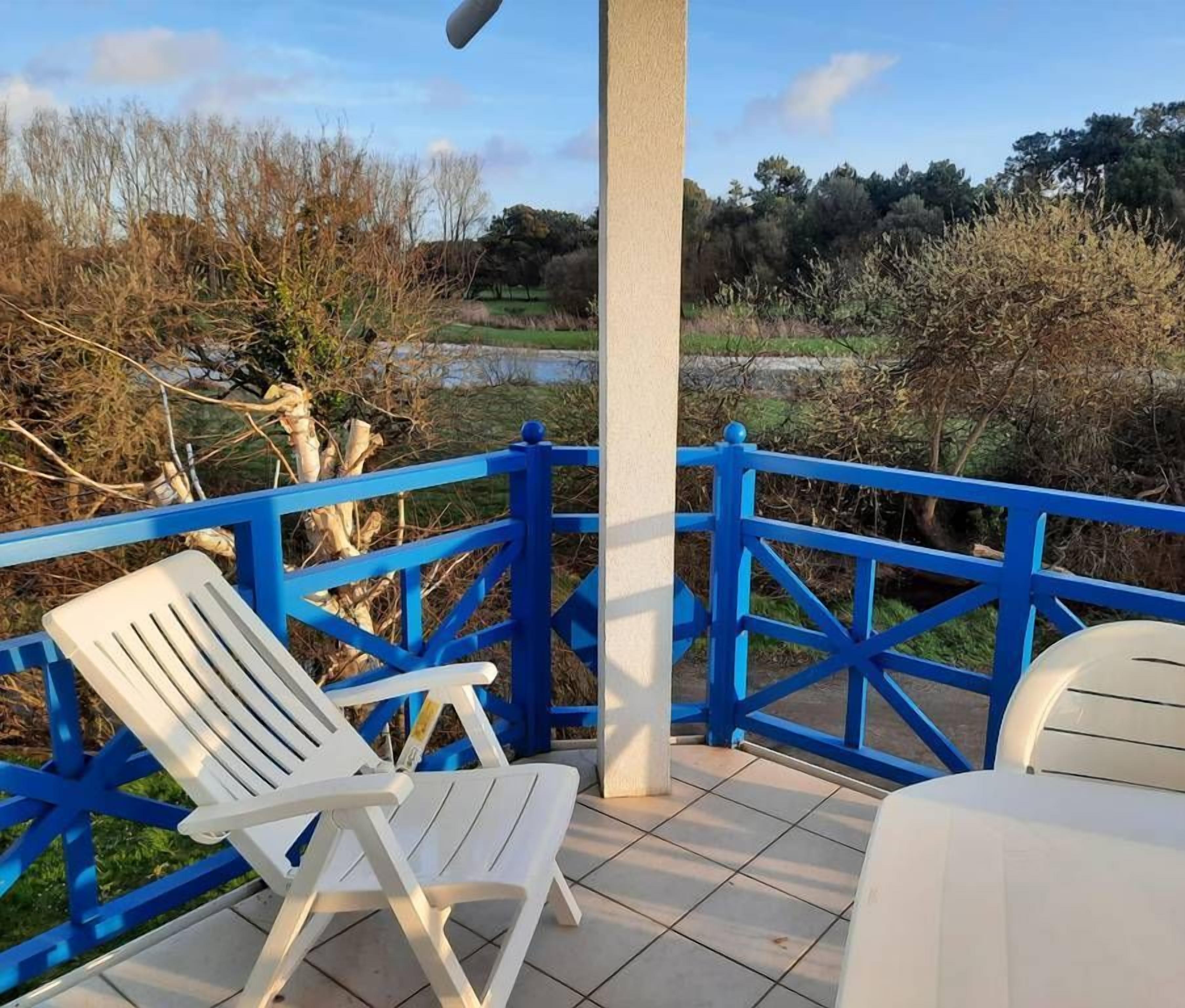 Een terras met een blauwe balustrade, twee witte stoelen en een tafel met een logo.