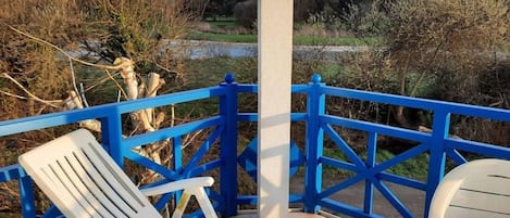 Una terraza con barandilla azul, dos sillas blancas y una mesa con un logotipo.