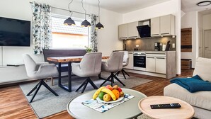 A modern living room with a dining area, kitchenette, and a TV mounted on the wall. - Cozy home in Lautenthal with sauna (Lautenthal)