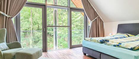 Ein Schlafzimmer mit großem Fenster, einem Bett, einem Sessel und einem Teppich.
