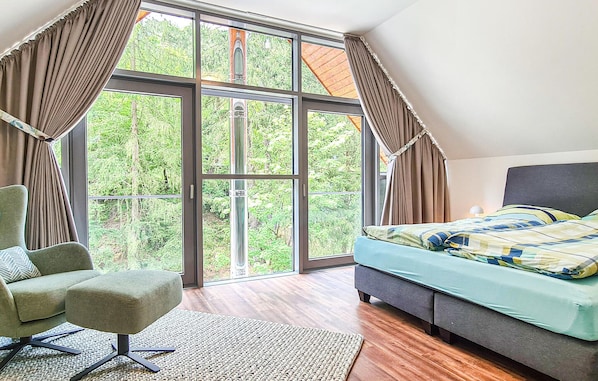A bedroom with a large window, a bed, a chair, and a rug. - Cozy home in Lautenthal with sauna (Lautenthal)