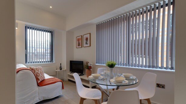 A modern living room with a glass dining table, white chairs, a sofa with a red throw, and a TV on a stand. - Apartment Sleeps 2 With Free Parking (Slough)