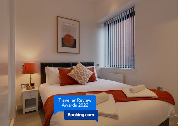 A modern hotel room with a neatly made bed, a bedside lamp, and a framed artwork on the wall.