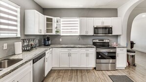 Una cocina moderna con armarios blancos, lavavajillas de acero inoxidable, microondas integrado y horno.