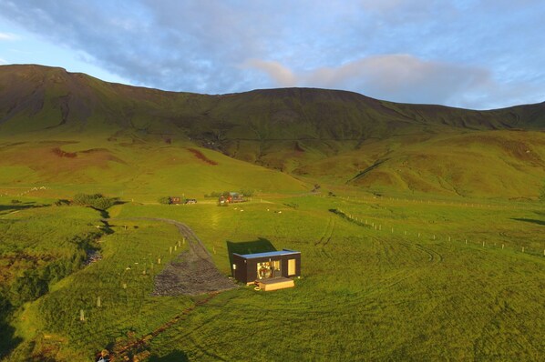 A remote, modern house in a lush green valley with rolling hills in the background. - Seljalandsfoss Cottage (Rangárþing eystra)