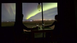 Two people seated at a table with a view of the Northern Lights. - Seljalandsfoss Cottage (Rangárþing eystra)