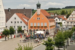 A traditional European town square with a prominent orange building featuring a clock tower, surrounded by white and red-roofed buildings. - HoLiDay ApartMENT Allgäu (Ottobeuren)