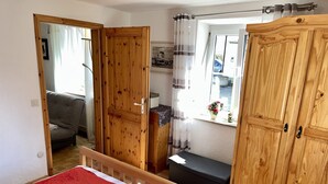 Een slaapkamer met een houten garderobe, een bed met rode beddengoed, een klein tafeltje en een raam met gordijnen.