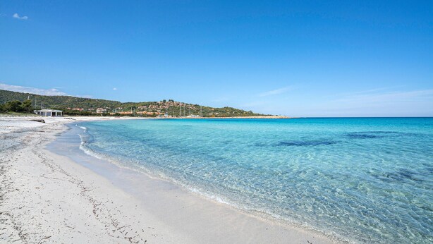 A beach with clear turquoise water, a sandy shore, and a hillside with buildings in the background. - 1 bedroom nice apartment in Budoni (Budoni)