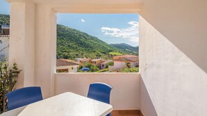A balcony with a table and chairs, overlooking a hillside village with terracotta-roofed buildings. - 1 bedroom nice apartment in Budoni (Budoni)