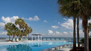Una piscina con sillas de descanso y palmeras, un pérgola y vistas al océano.