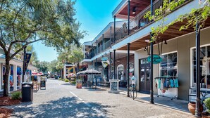 Calle bordeada de tiendas y cafés, con mesas al aire libre y cielo despejado.