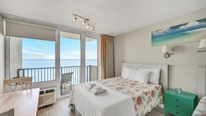 Un dormitorio con cama, escritorio, silla, mesita de noche y vista al mar.