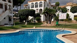 A swimming pool with a curved edge, surrounded by a paved area and a building with arched windows and a tiled roof. - Spacious and bright apartment 700m from the beach (VC)