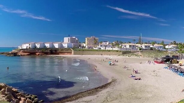 A beach with clear blue water, a sandy shore, and buildings in the background. - Spacious and bright apartment 700m from the beach (VC)