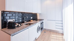 A modern kitchen with white cabinets, a granite countertop, a built-in washing machine, and a black backsplash.