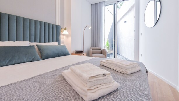 A modern hotel room with a large bed, a chair, a desk, and a view of the outdoors.