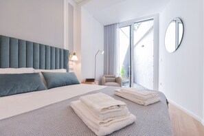 A modern hotel room with a large bed, a chair, a desk, and a view of the outdoors.