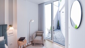 A modern room with a bed, a chair, a desk with a lamp, and a large window.