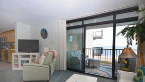 A living room with a television, a sofa, a coffee table, and a balcony with a view of the sea.