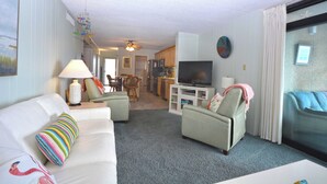 A living room with a white sofa, a television, and a dining area in the background.