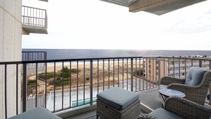 A balcony with wicker furniture, a view of the beach, and a swimming pool.